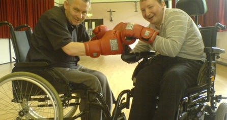 Two people who use wheelchairs with boxing gloves